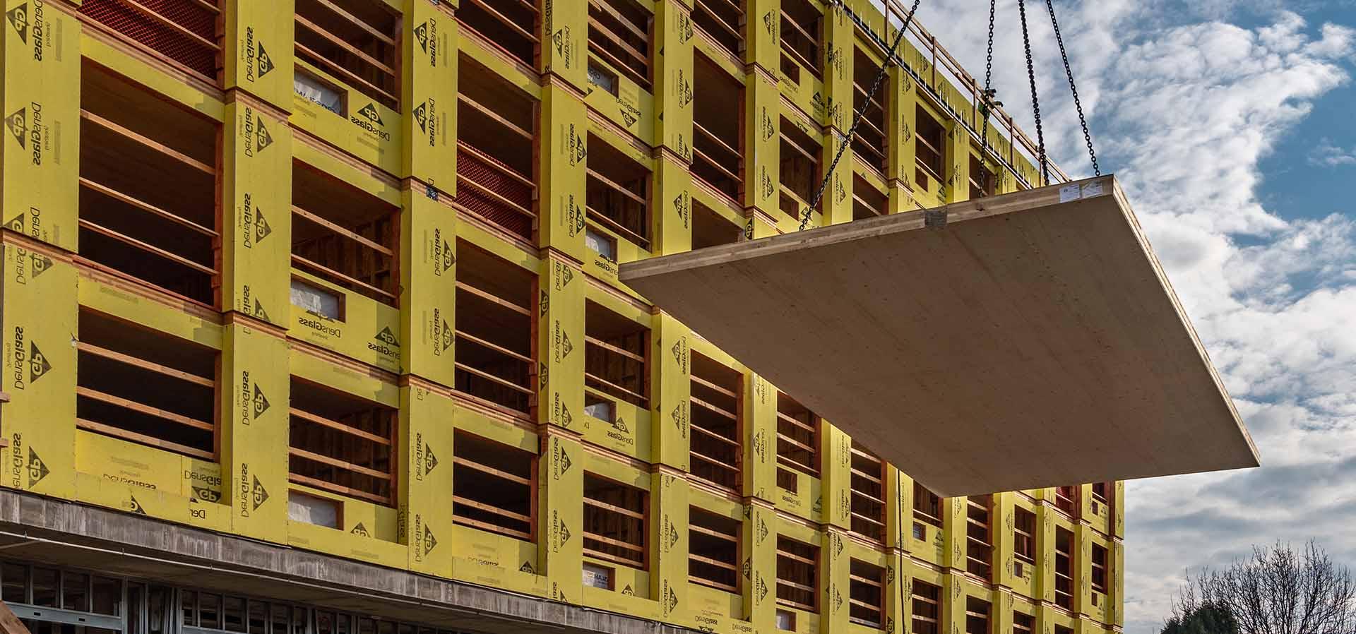 CLT panel being flown in on a crane in front of a mass timber building